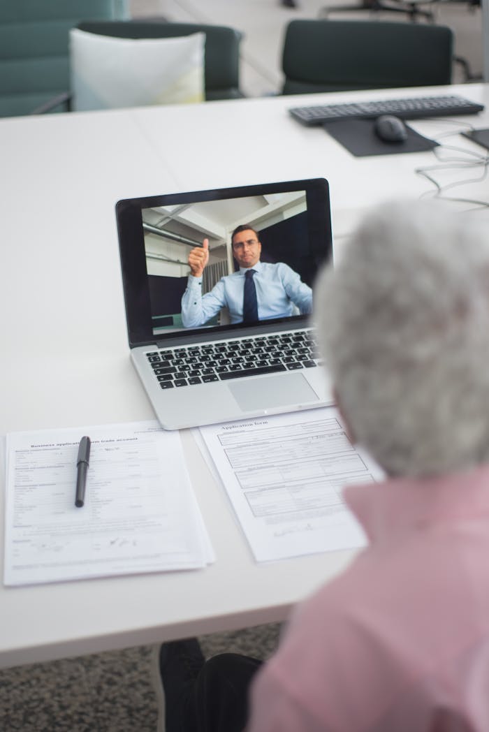 Senior man engages in a video conference with a colleague on a laptop, discussing documents.